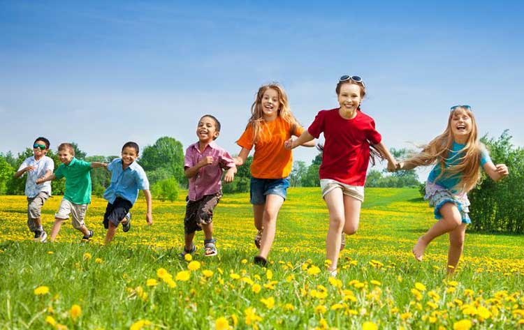 children of various ages running in a field of grass with dandelions